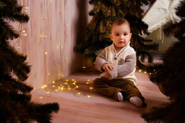 Um menino perto das árvores de Natal em um trenó, luzes de Natal, alegrias e sorrisos, peças de teatro. férias e férias — Fotografia de Stock