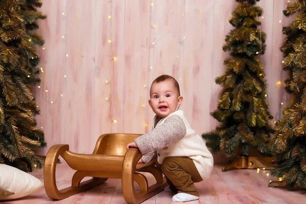 Um menino perto das árvores de Natal em um trenó, luzes de Natal, alegrias e sorrisos, peças de teatro. férias e férias — Fotografia de Stock