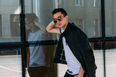 Sokakta güneş gözlükleriyle duran çekici, seksi adam. Kendine güven, gaz çıkarma ve kibir. Model, poz, genç bir adamın portresi.