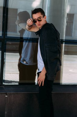 Sokakta güneş gözlükleriyle duran çekici, seksi adam. Kendine güven, gaz çıkarma ve kibir. Model, poz, genç bir adamın portresi.