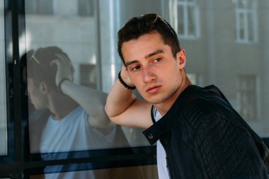 Sokakta güneş gözlükleriyle duran çekici, seksi adam. Kendine güven, gaz çıkarma ve kibir. Model, poz, genç bir adamın portresi.