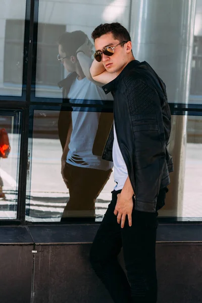 Un tipo atractivo y sexy parado en la calle con gafas de sol. confianza en sí mismo, flatulencia y arrogancia. modelo, posesion, retrato de un joven — Foto de Stock