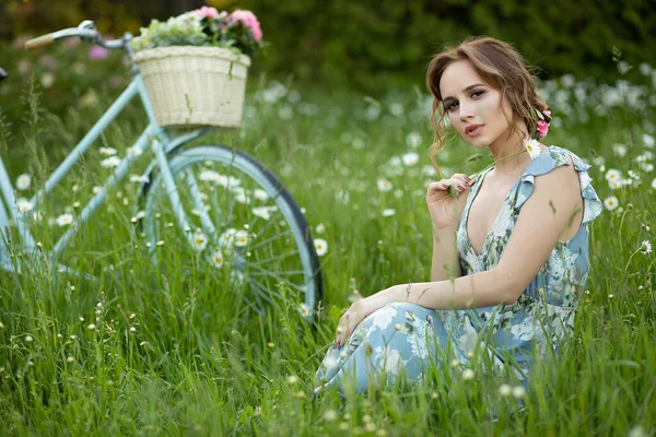 Portret pięknej dziewczyny w lesie, trzymając rower z koszem kwiatów, za promieniami słońca, niebieską kwiecistką sukienkę, letni spacer — Zdjęcie stockowe