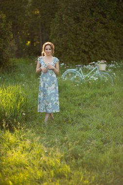 Yazın gün batımında güzel bir kız elinde çiçekle bir tarlada, yazın yürüyor, gidiyor, güneş parlıyor.