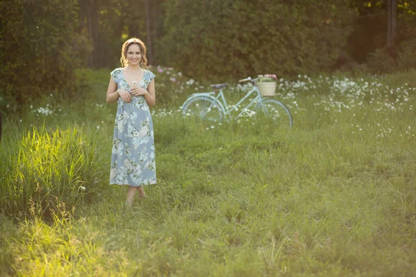 Menina bonita ao pôr do sol no verão em um campo com uma flor na mão, caminha no verão, vai, o sol está brilhando — Fotografia de Stock