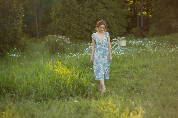 Vacker flicka vid solnedgången på sommaren i ett fält med en blomma i handen, promenader på sommaren, går, solen skiner — Stockfoto