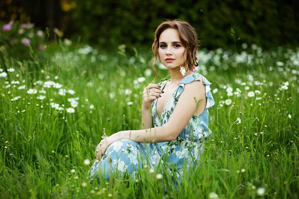 Hermosa chica al atardecer en verano en un campo con una flor en la mano, camina en el verano, va, el sol está brillando — Foto de Stock