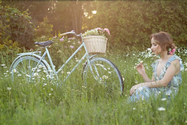 La bicicleta se para en un día de verano en el campo, una chica con una flor se sienta cerca — Foto de Stock