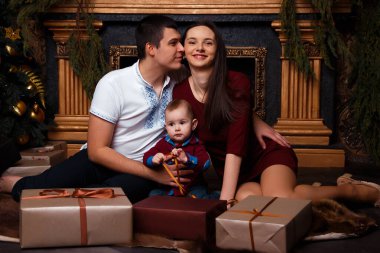 Hediye kutuları olan aile Noel ağacının yanında oturur, gülüp oynarlar, aile mutluluğu, şömine, kalplerin sıcaklığı.