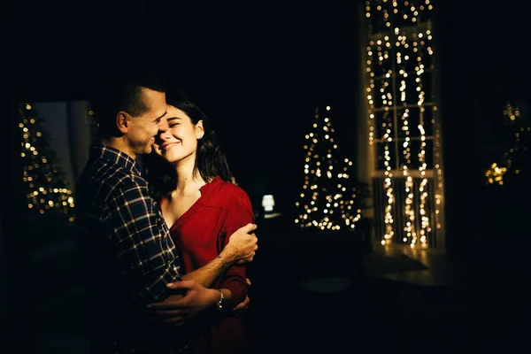 Felice, coppia innamorata al buio, sera sul divano, sfondo scuro, luci dell'albero di Natale. Serata di Natale. Capodanno. abbraccio e bacio. attrazione, serata romantica e appuntamento . — Foto Stock