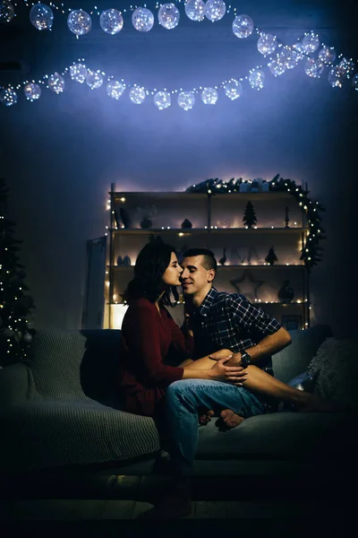 Щаслива, закохана пара в темряві, ввечері на дивані, на темному тлі, ялинкові вогні. Новорічний вечір. Новий рік. обійняти і поцілувати. атракціон, романтичний вечір і дата . — стокове фото