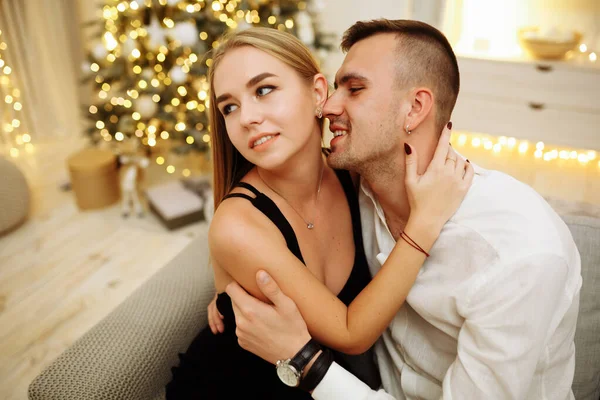 Verliebte Küsse und Umarmungen auf dem Sofa neben der Weihnachtsbaumbeleuchtung. Neujahrsnacht. Weihnachten. — Stockfoto