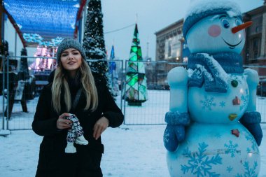 Kış şapkalı güzel bir kız Noel ağacının yanında, kış tatilleri, tatiller ve bir film fotoğrafının altında buğdayla yürüyor.