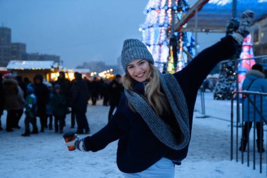 Kış şapkalı güzel bir kız Noel ağacının yanında, kış tatilleri, tatiller ve bir film fotoğrafının altında buğdayla yürüyor.