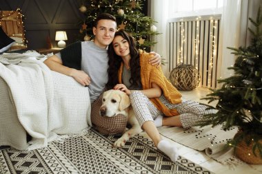 Mutlu çift yatağın yanında bir köpekle oturuyor, Noel 'de. Evde yeni yıl. aile ve tarih