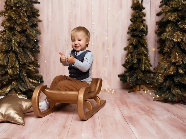 Un garçon près des arbres de Noël sur un traîneau, lumières de Noël, se réjouit et sourit, joue. vacances et vacances — Photo