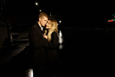 Geceler, yağmurlar, şehirdeki binalar, gülücükler, cazibe. Adam kıza sarılıyor. Sevgililer Günü