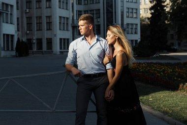 Mutlu çift kucaklaşıyorlar ve şehrin önünde duruyorlar. Karanlık arka plan, güneş aşıkların üzerine parlıyor.