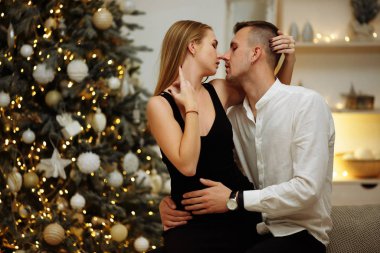 Birbirine aşık çiftler Noel ağacı ışıklarının yanındaki kanepede öpüşüp sarılıyorlar. Yılbaşı gecesi. Noel.