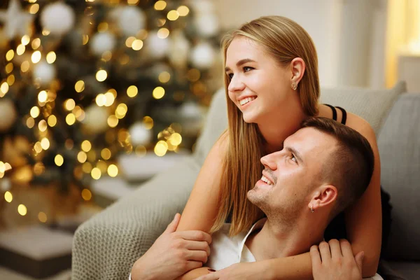 Verliebte Küsse und Umarmungen auf dem Sofa neben der Weihnachtsbaumbeleuchtung. Neujahrsnacht. Weihnachten. — Stockfoto