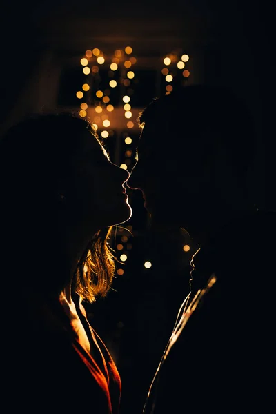 Силуэт мужчины и женщины на фоне огней в темноте, контур лица, целующаяся пара в огнях праздника, любовь и романтика. Новый год и Рождество . — стоковое фото