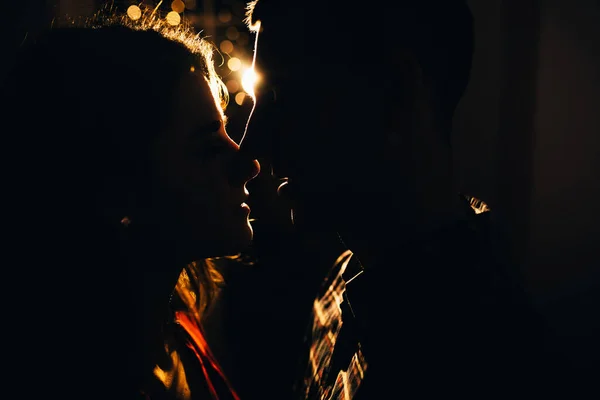 Silhouet van een man en een vrouw op een achtergrond van licht in het donker, contour van het gezicht, een zoenend koppel in het licht van de vakantie, liefde en romantiek. Oudejaarsavond en Kerstmis. — Stockfoto