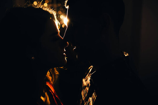 silhouette of a man and a woman on a background of lights in the dark, contour of the face, a kissing couple in the lights of the holiday, love and romance. New Year's Eve and Christmas.