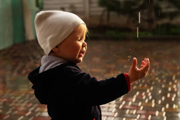 Een klein kind vangt regendruppels, spettert in zijn gezicht, sluit zijn ogen. regenachtig weer. nat weer. kennis maken met de wereld. — Stockfoto