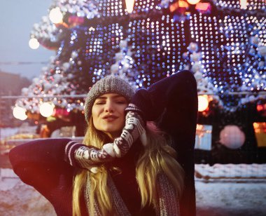 Kış şapkalı güzel bir kız Noel ağacının yanında, kış tatilleri, tatiller ve bir film fotoğrafının altında buğdayla yürüyor.