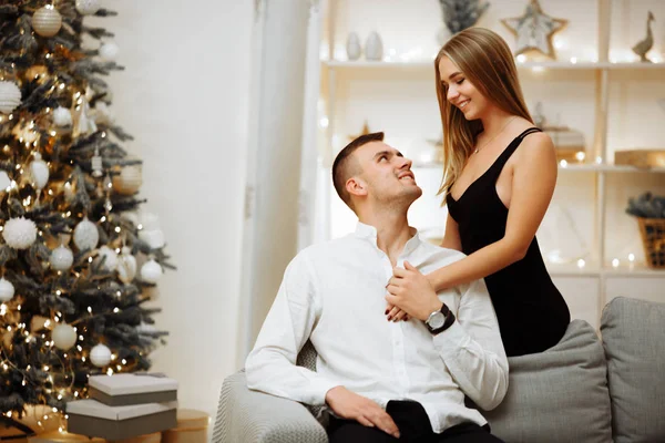 恋爱中的夫妻在圣诞树前的沙发上亲吻拥抱。 新年的夜晚。 圣诞节. — 图库照片