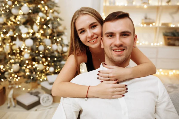 Par förälskade kyssar och kramar på soffan nära julgransljuset. Nyårsnatten. Julen. — Stockfoto