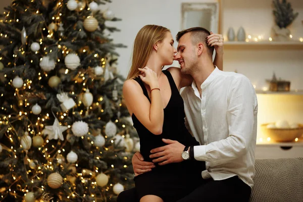 クリスマスツリーのライトの近くのソファにキスと抱擁でカップル。新年の夜。クリスマス. — ストック写真