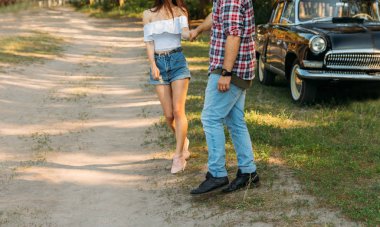 Siyah bir arabanın arka planında duran bir çift, arabanın kapısına dayanan bir adam. Dikey fotoğraf.