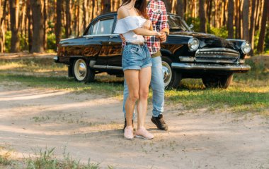 Siyah bir arabanın arka planında duran bir çift, arabanın kapısına dayanan bir adam. Dikey fotoğraf.