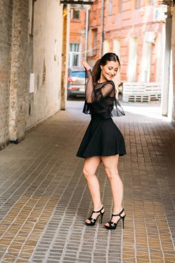 Kız gülümsüyor. Moda 'nın güzel genç bir bayanın duygusal portresi. Şehir portresi. Siyah elbiseli esmer. Beklenti. hayaller