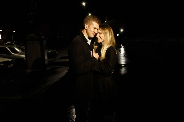 Casal apaixonado abraçando contra um fundo escuro, noite, chuva, edifícios na cidade, um parque, sorrindo, atração. O tipo abraçou a rapariga. Dia dos Namorados — Fotografia de Stock