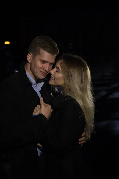 Casal apaixonado abraçando contra um fundo escuro, noite, chuva, edifícios na cidade, um parque, sorrindo, atração. O tipo abraçou a rapariga. Dia dos Namorados — Fotografia de Stock