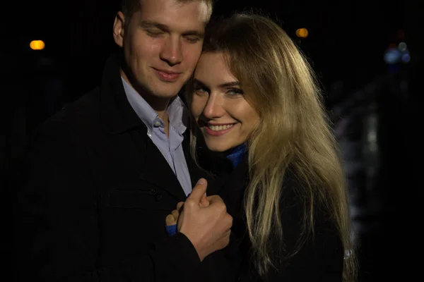 Verliebte Paare umarmen sich vor dunklem Hintergrund, Nacht, Regen, Gebäude in der Stadt, ein Park, lächelnd, Attraktion. der Kerl umarmt das Mädchen. Valentinstag — Stockfoto