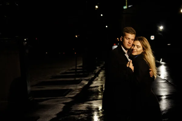 Coppia innamorata che si abbraccia su uno sfondo scuro, notte, pioggia, edifici in città, un parco, sorridente, attrazione. Il ragazzo abbraccia la ragazza. San Valentino — Foto Stock