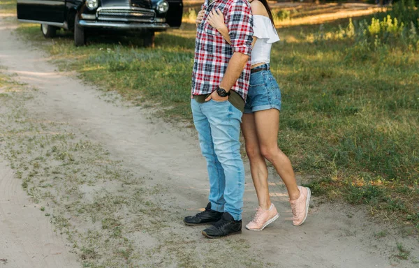 A couple standing hugs against the backdrop of a black car, a man leaning on the car door.vertical photo — Stock Photo, Image