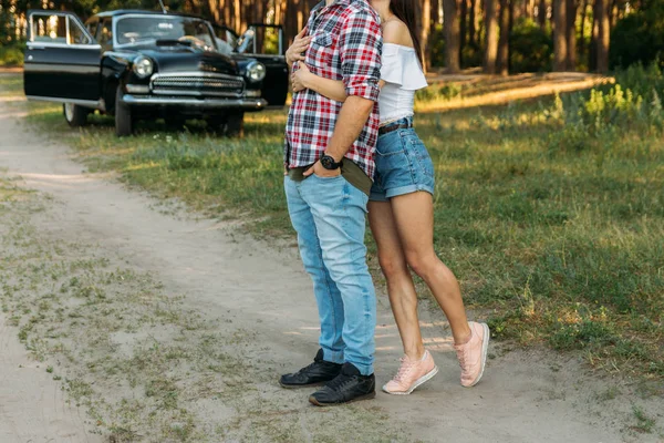 A couple standing hugs against the backdrop of a black car, a man leaning on the car door.vertical photo — 스톡 사진