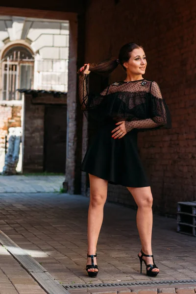 La chica está posando sonrisas. Retrato emocional de moda retrato elegante de mujer joven y bonita. retrato de la ciudad. morena en un vestido negro. expectativa. sueños — Foto de Stock