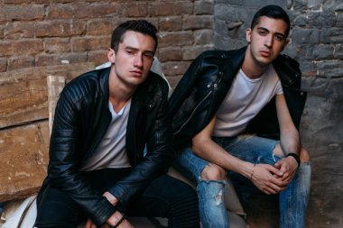 beautiful and attractive guy sit on white bags against a brick wall, construction in the city, posing. walk around the city. communication. meeting friends.