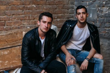 beautiful and attractive guy sit on white bags against a brick wall, construction in the city, posing. walk around the city. communication. meeting friends.