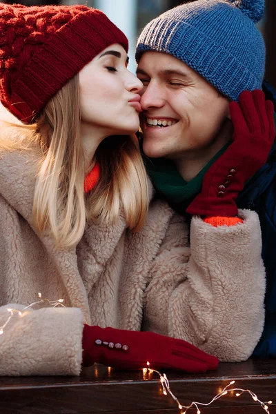 恋愛カップルは恋人も女の子も目を閉じた少女が鼻で男にキスをすると男は微笑む頬を撫でてバーガンディ帽子と手袋冬. — ストック写真
