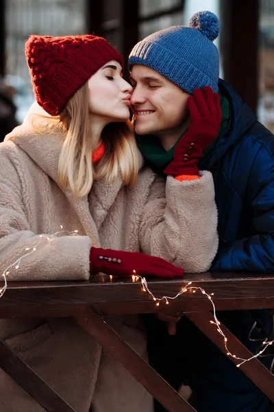 Romance couple in love, girl and boyfriend. the girl with closed eyes kisses the guy in the nose, the man smiles. stroking her cheek. burgundy hat and gloves, winter. — Stok fotoğraf