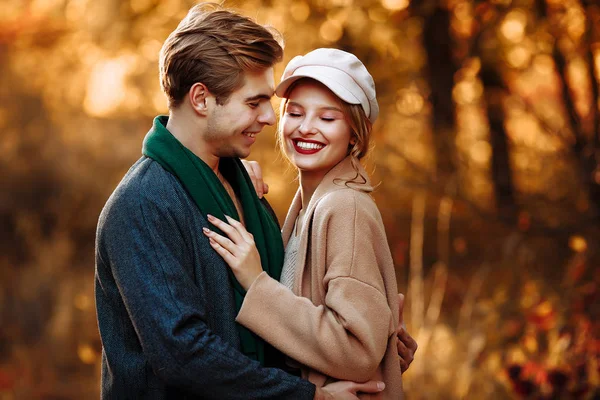 Felice, coppia innamorata abbracci e sorrisi per strada, autunno, sciarpa verde e cappello, uomo e donna su un appuntamento, giorno di San Valentino. passeggiata nel parco — Foto Stock