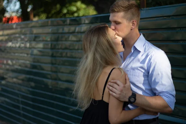 Мужчина целует девушку на улице, обнимает ее, привлекает друг друга. девушка в черном платье и улыбается — стоковое фото