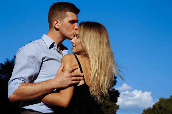 Uomo bacia una ragazza per strada, abbracciandola, attratto l'uno dall'altro. ragazza in abito nero e sorridente — Foto Stock