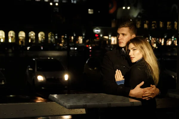 couple in love embracing against a dark background, night, rain, buildings in the city, a park, smiling,attraction. the guy hugs the girl. Valentine's Day dark street and rain